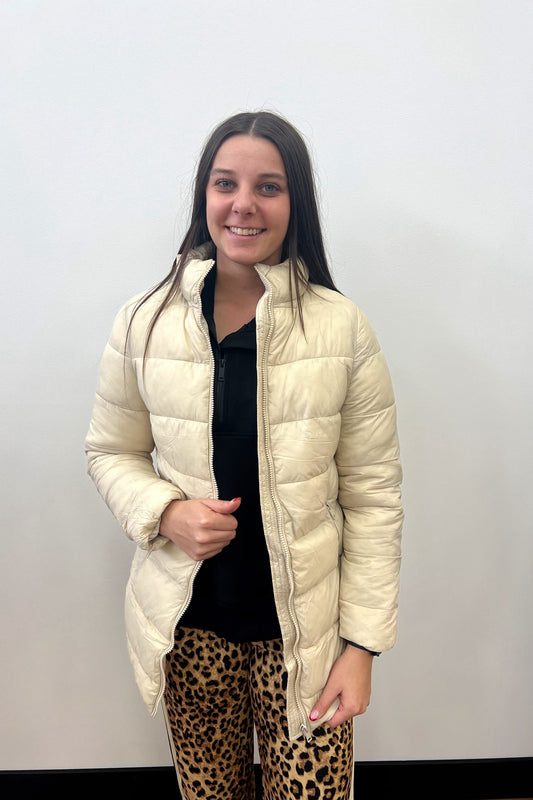 Person wearing a beige puffer jacket and leopard print pants against a plain background