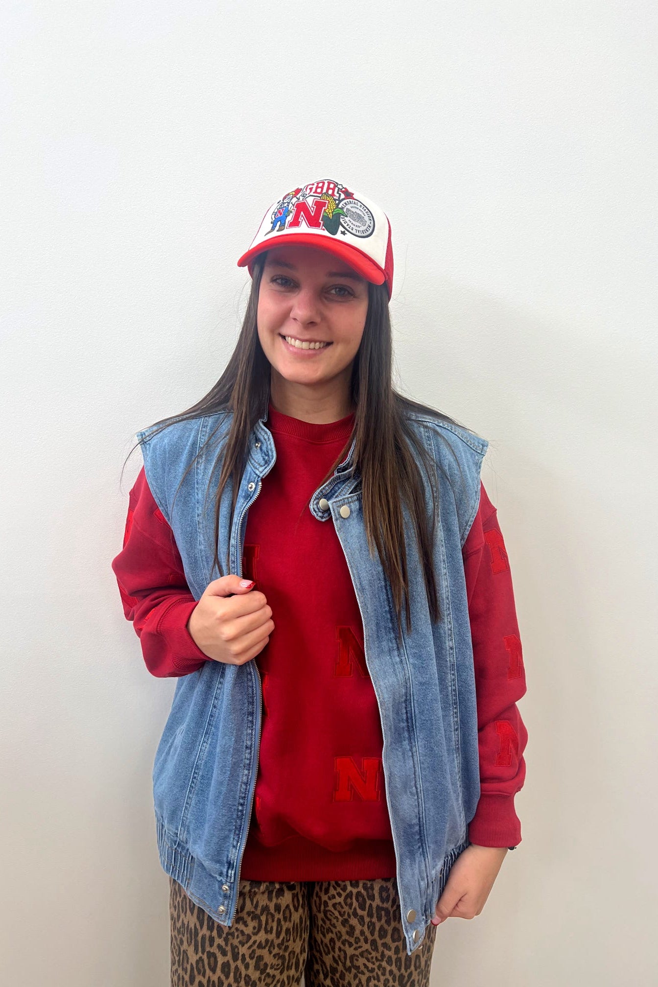 Person wearing a red cap, denim vest, and red shirt against a white background
