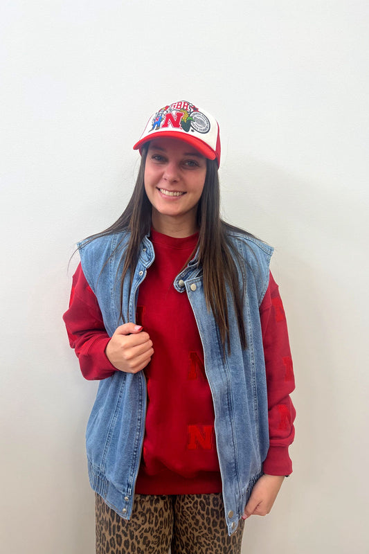 Person wearing a red cap, denim vest, and red shirt against a white background