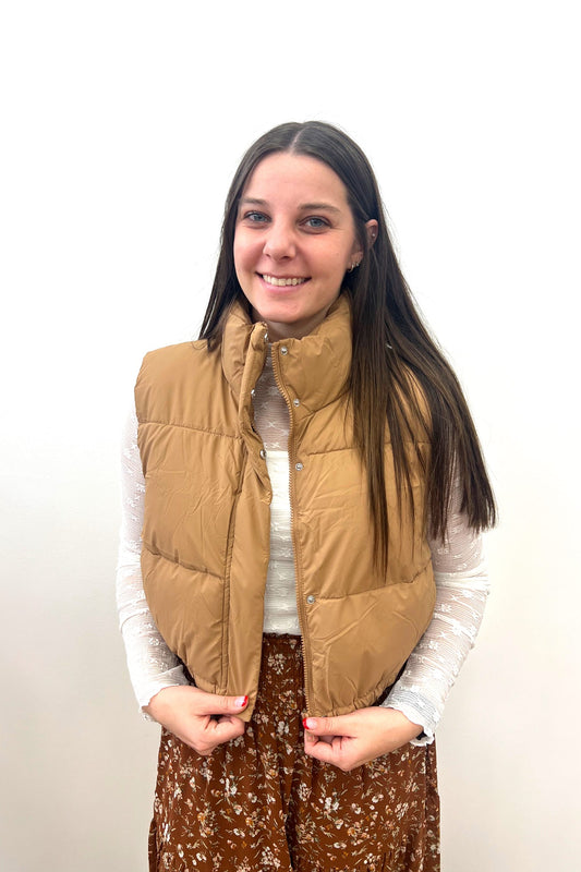 Woman wearing a tan puffer vest against a white background