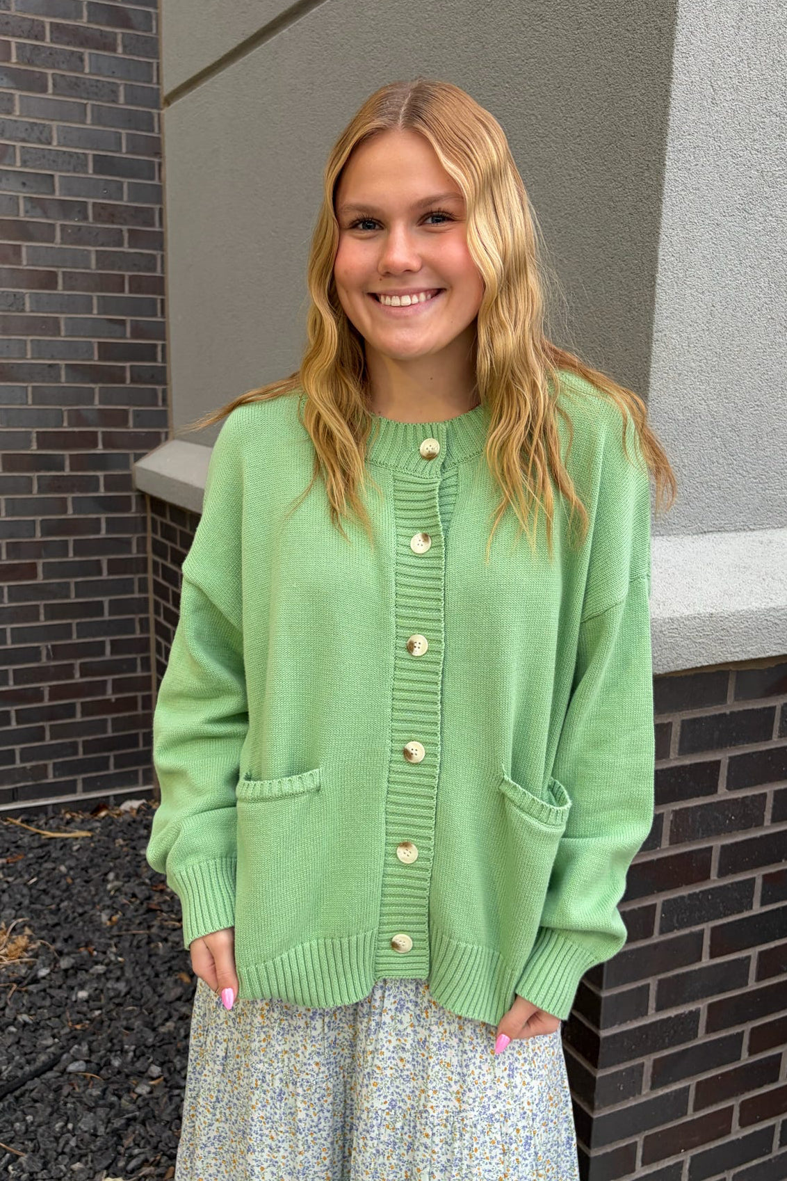 Woman wearing a green cardigan standing against a brick wall.