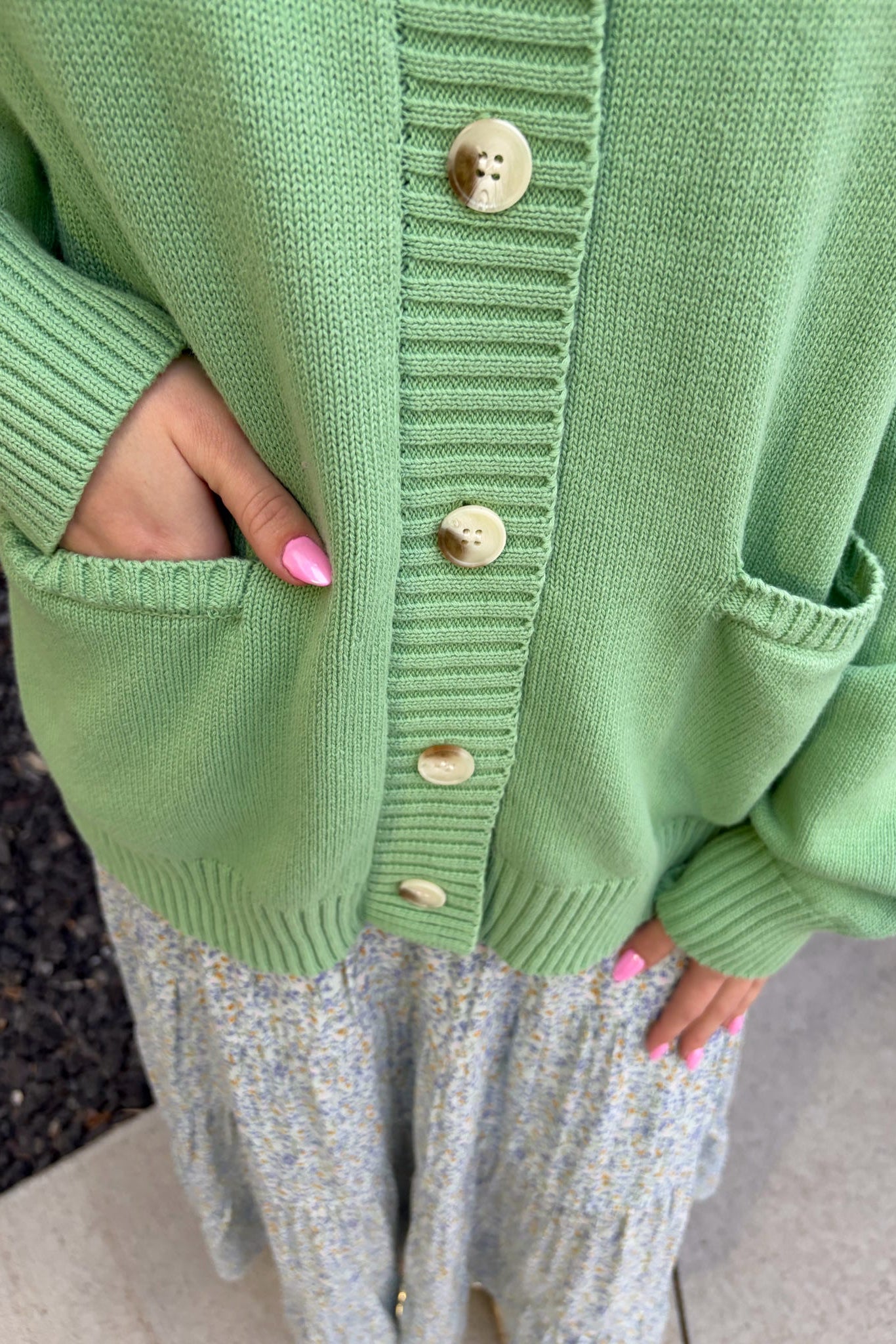 Green cardigan with button details worn by a person, with a blurred background.