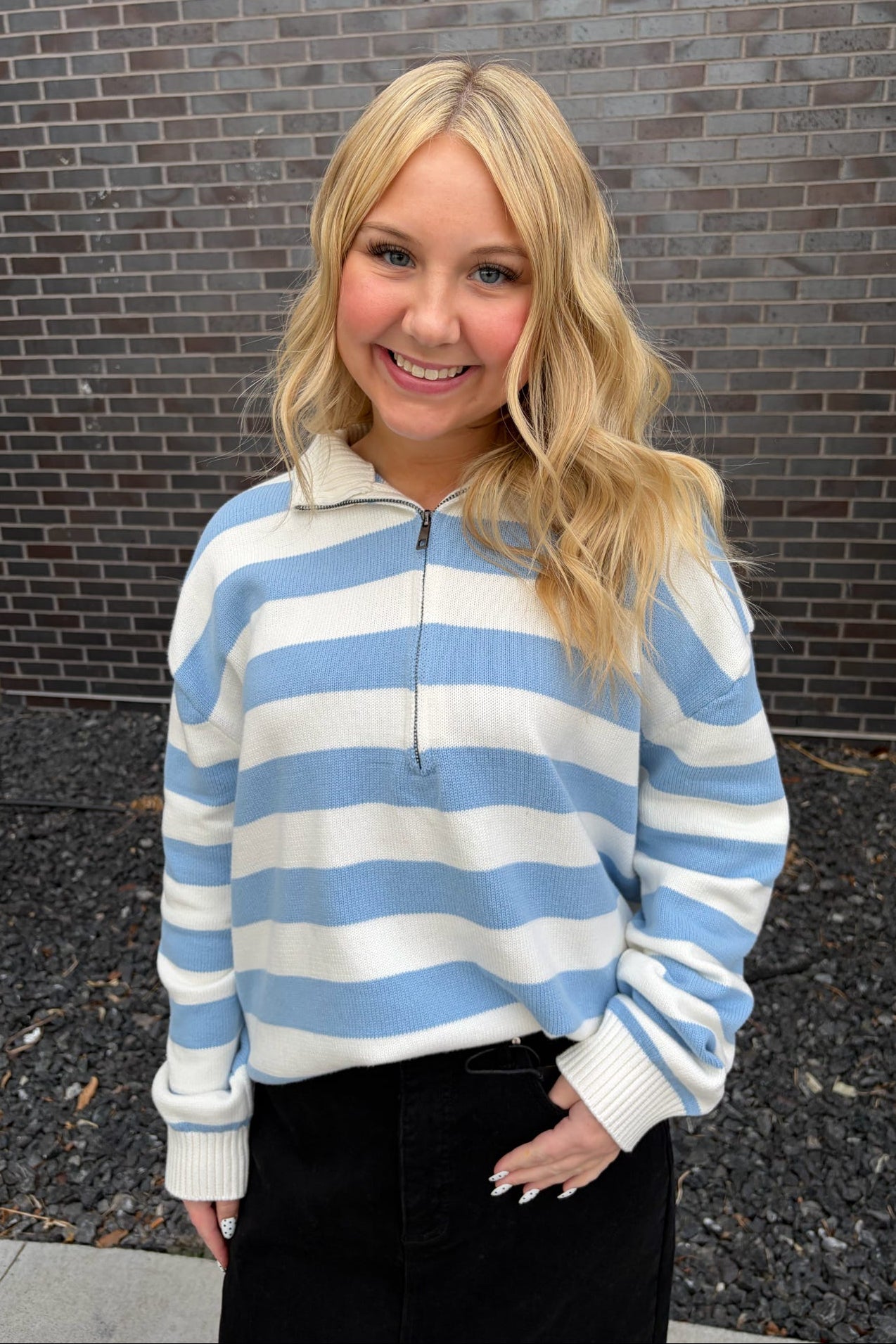 Woman wearing a blue and white striped sweater standing in front of a brick wall.