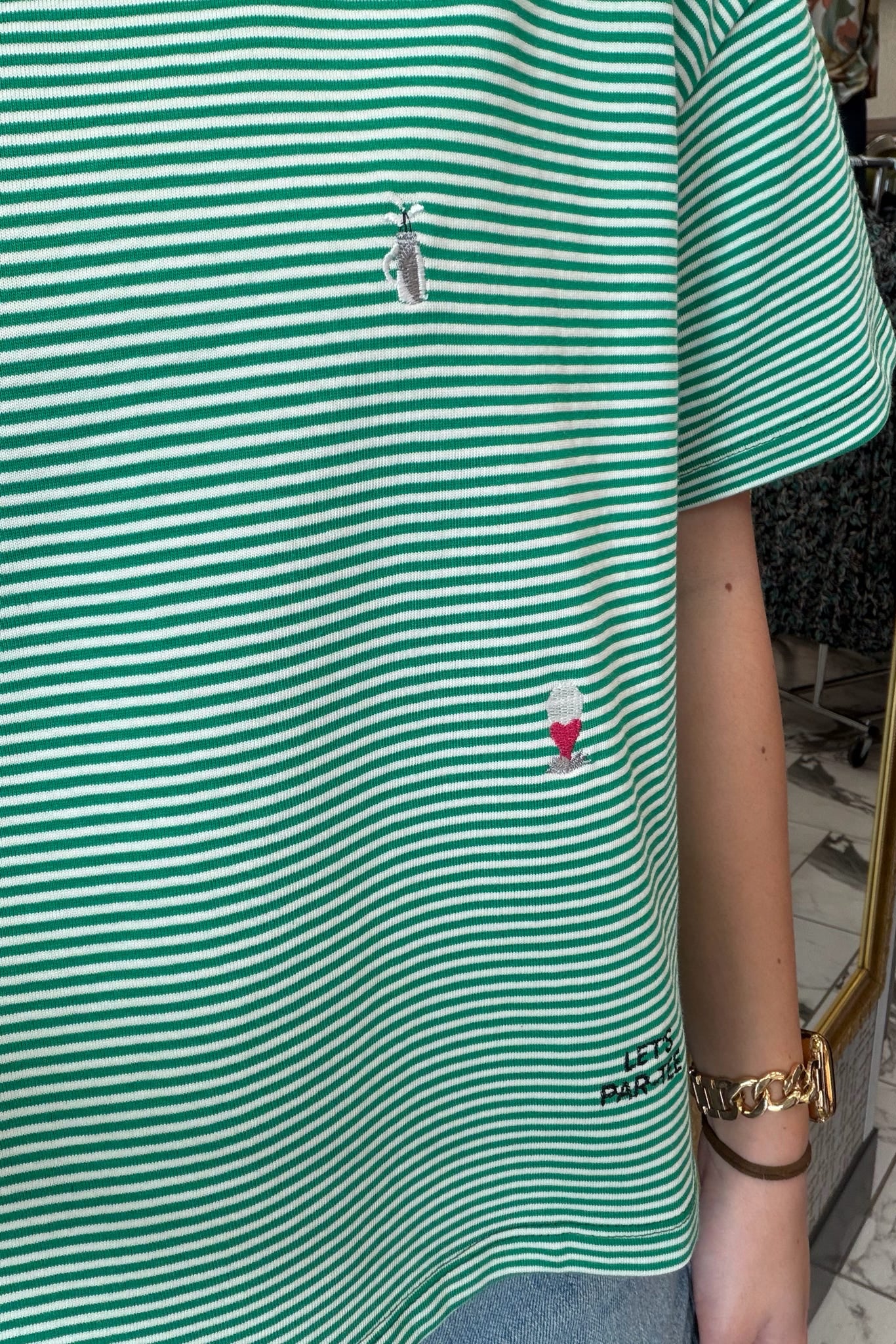 Green and white striped shirt with a small embroidered design, worn by a person.