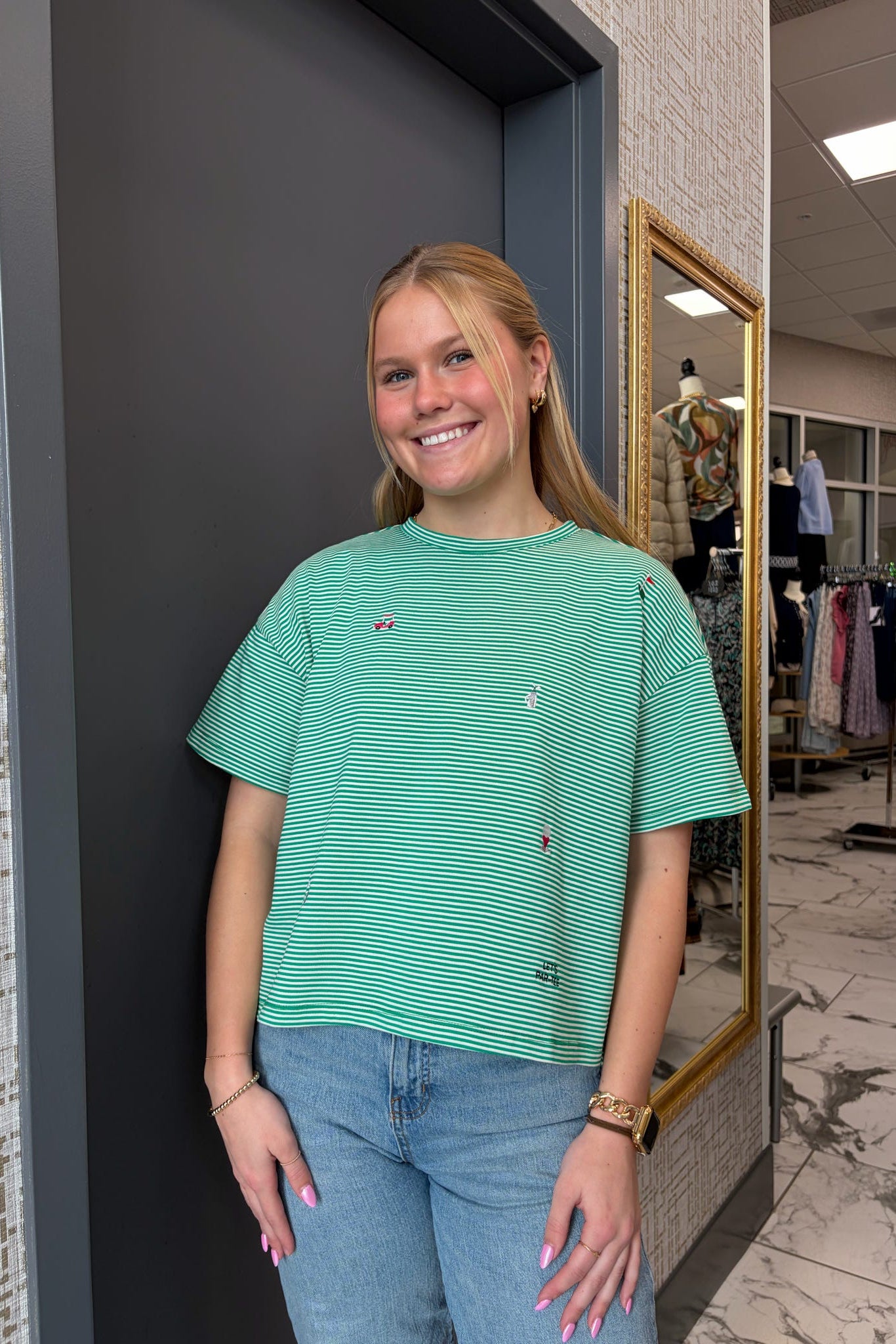 Woman wearing a green striped shirt and blue jeans standing in a store.