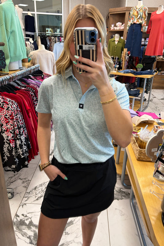 Person taking a mirror selfie in a clothing store wearing a light blue polo shirt and black skirt.