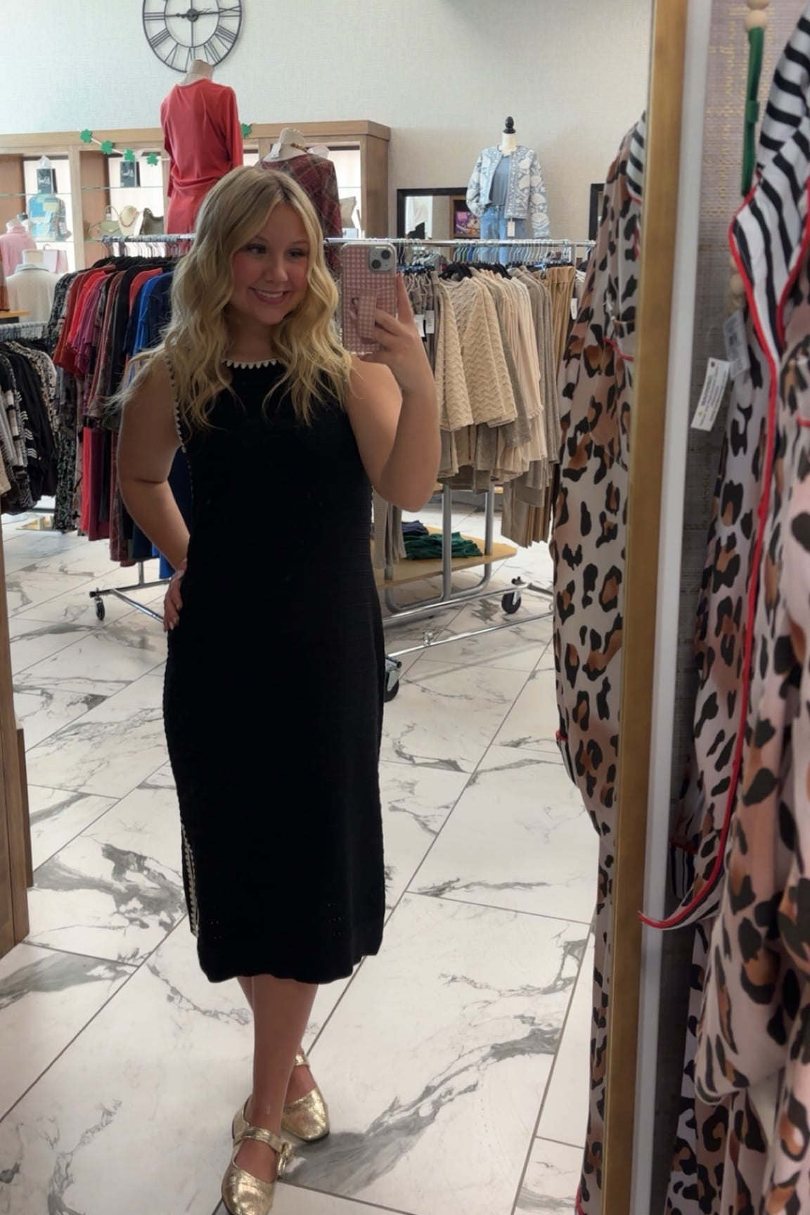 Woman taking a mirror selfie wearing a black dress in a clothing store.