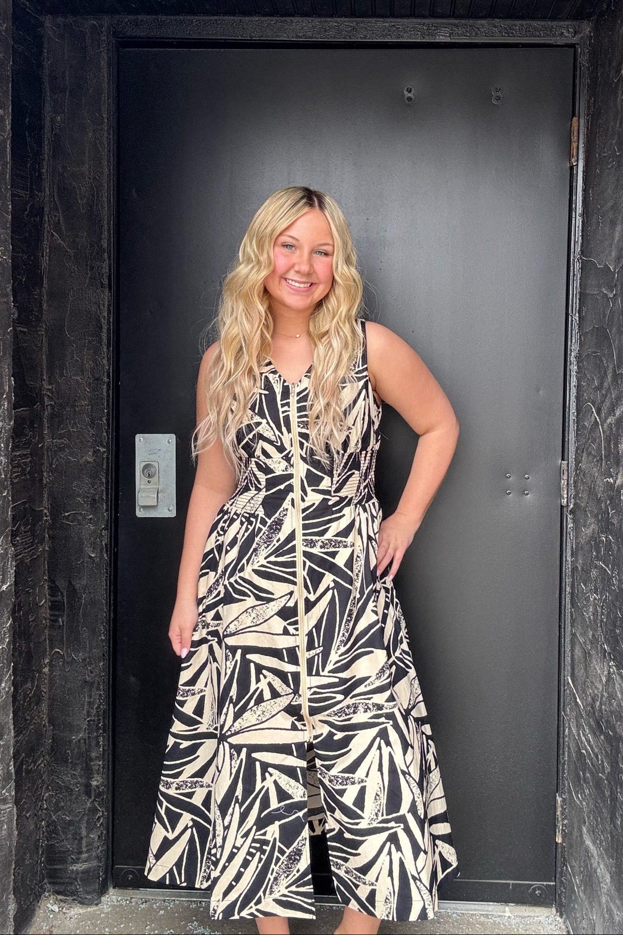 Woman in a patterned dress standing in front of a black door.