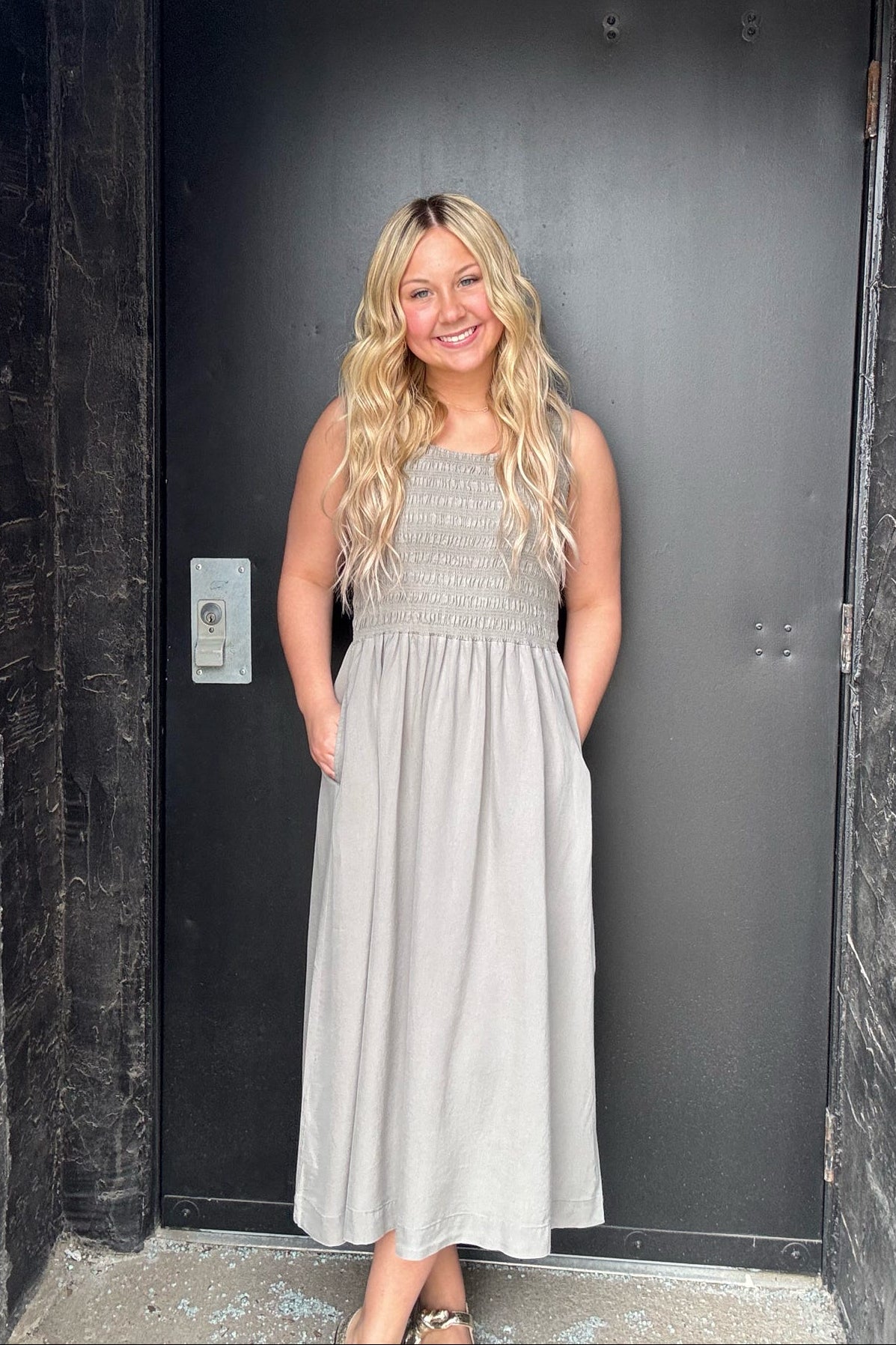 Woman in a gray dress standing in front of a black door.