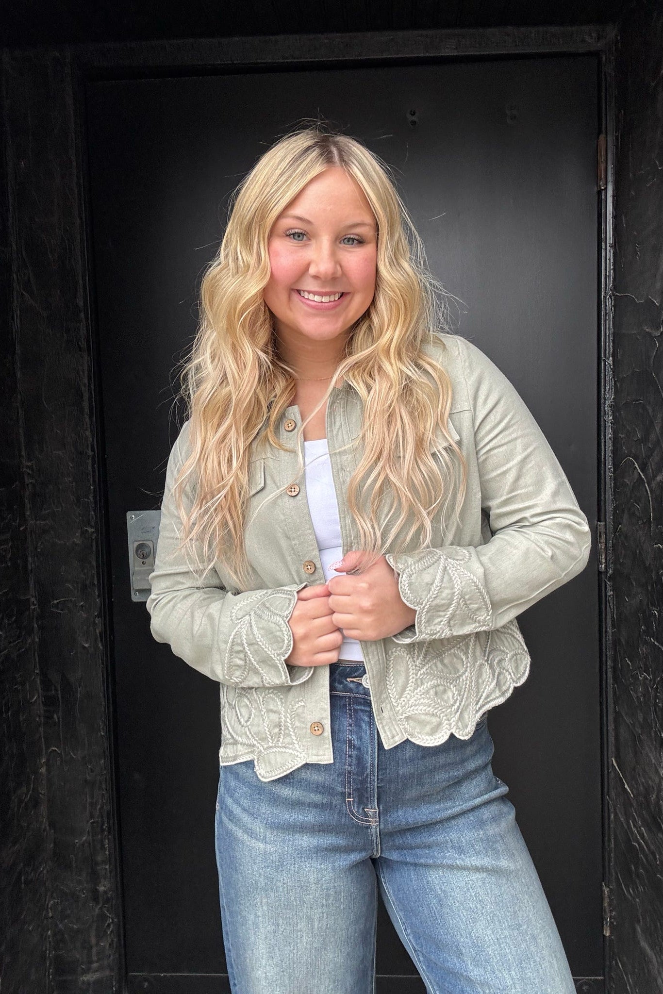 Woman wearing a light-colored jacket and jeans standing against a dark background