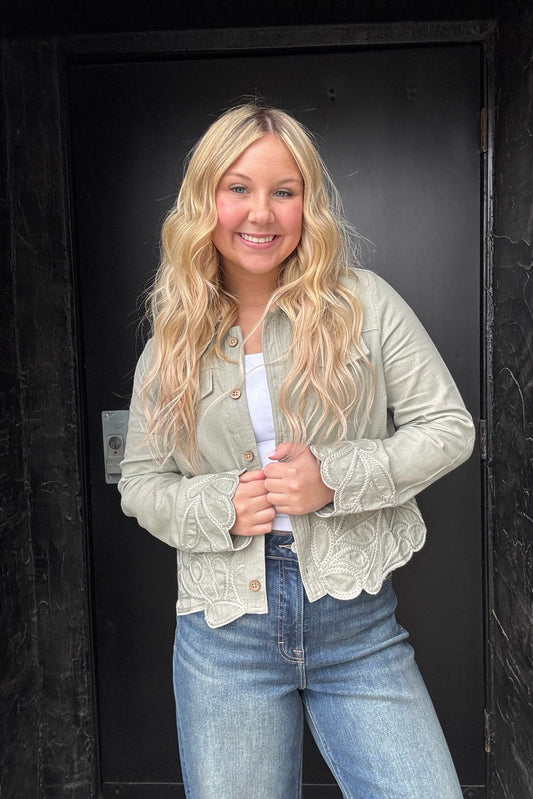 Woman wearing a light-colored jacket and jeans standing against a dark background