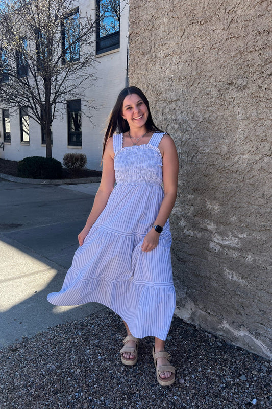 Woman in a white and blue striped dress standing against a building.