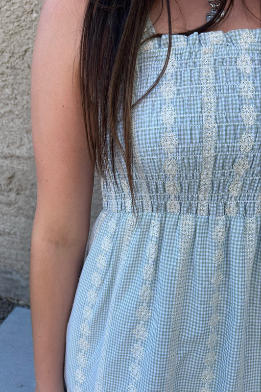 Person wearing a blue checkered dress against a concrete wall.