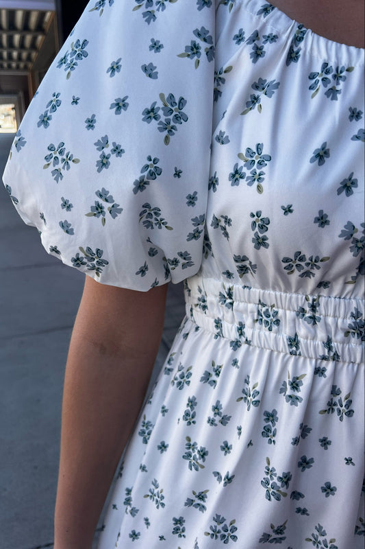 White dress with blue floral pattern worn by a person on a street.