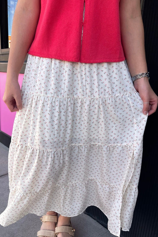 Person wearing a red top and white floral skirt on a city street.