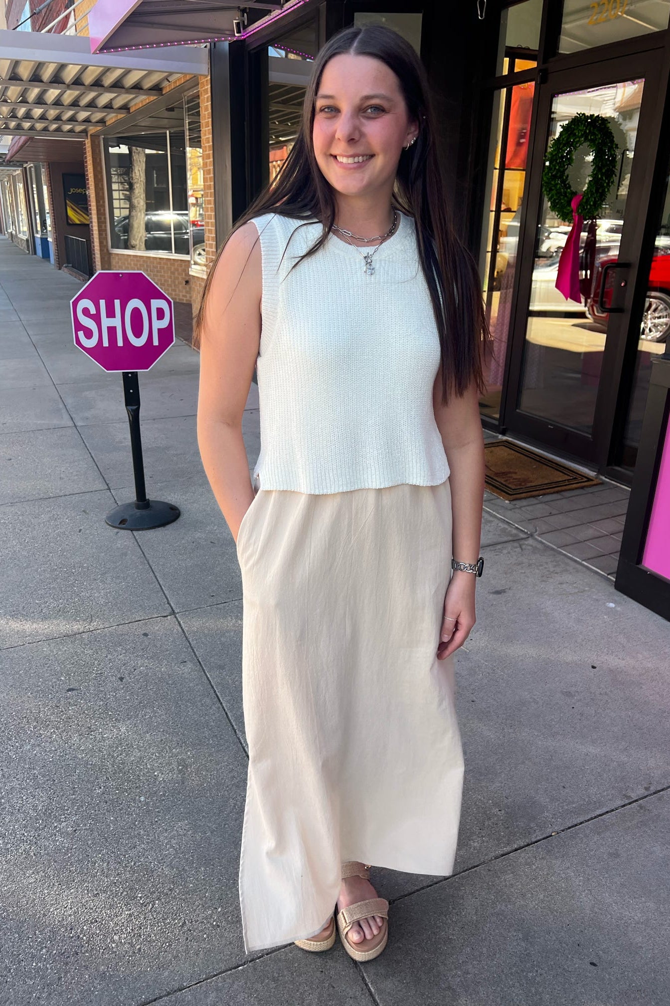 Woman standing on a sidewalk with a 'Shop' sign in the background