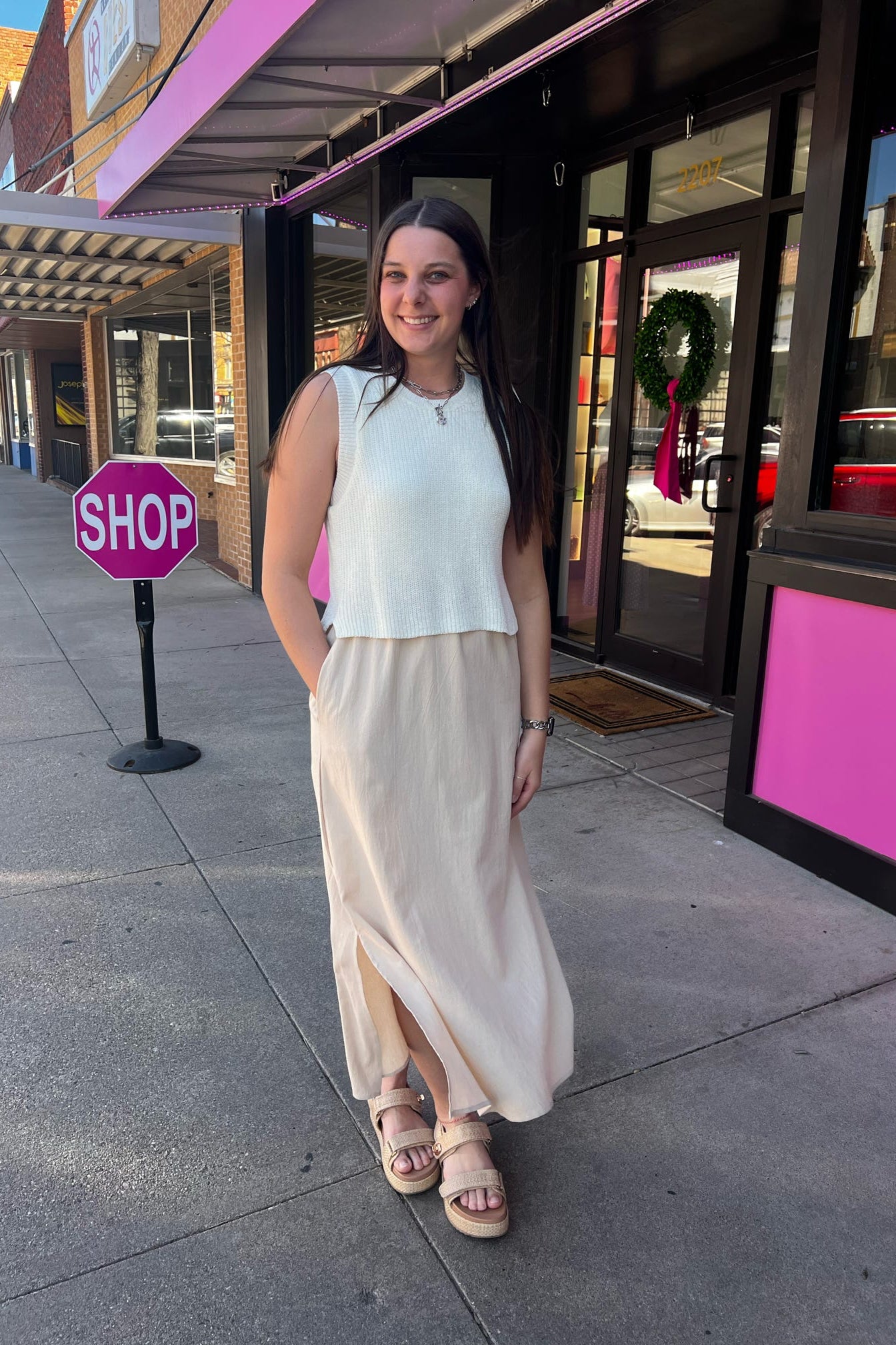 Woman standing on a sidewalk next to a 'STOP' sign with a store in the background