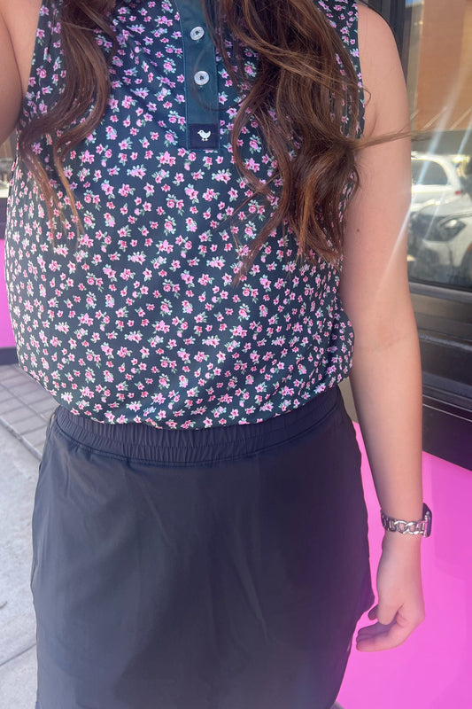 Person wearing a sleeveless floral top and dark pants on a pink floor.