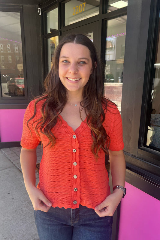 Woman wearing an orange cardigan standing outside a building with pink accents.