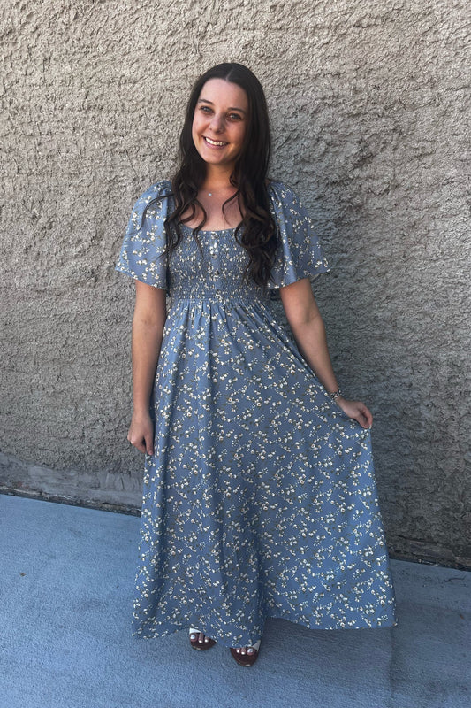 Woman in a blue floral dress standing against a textured wall.