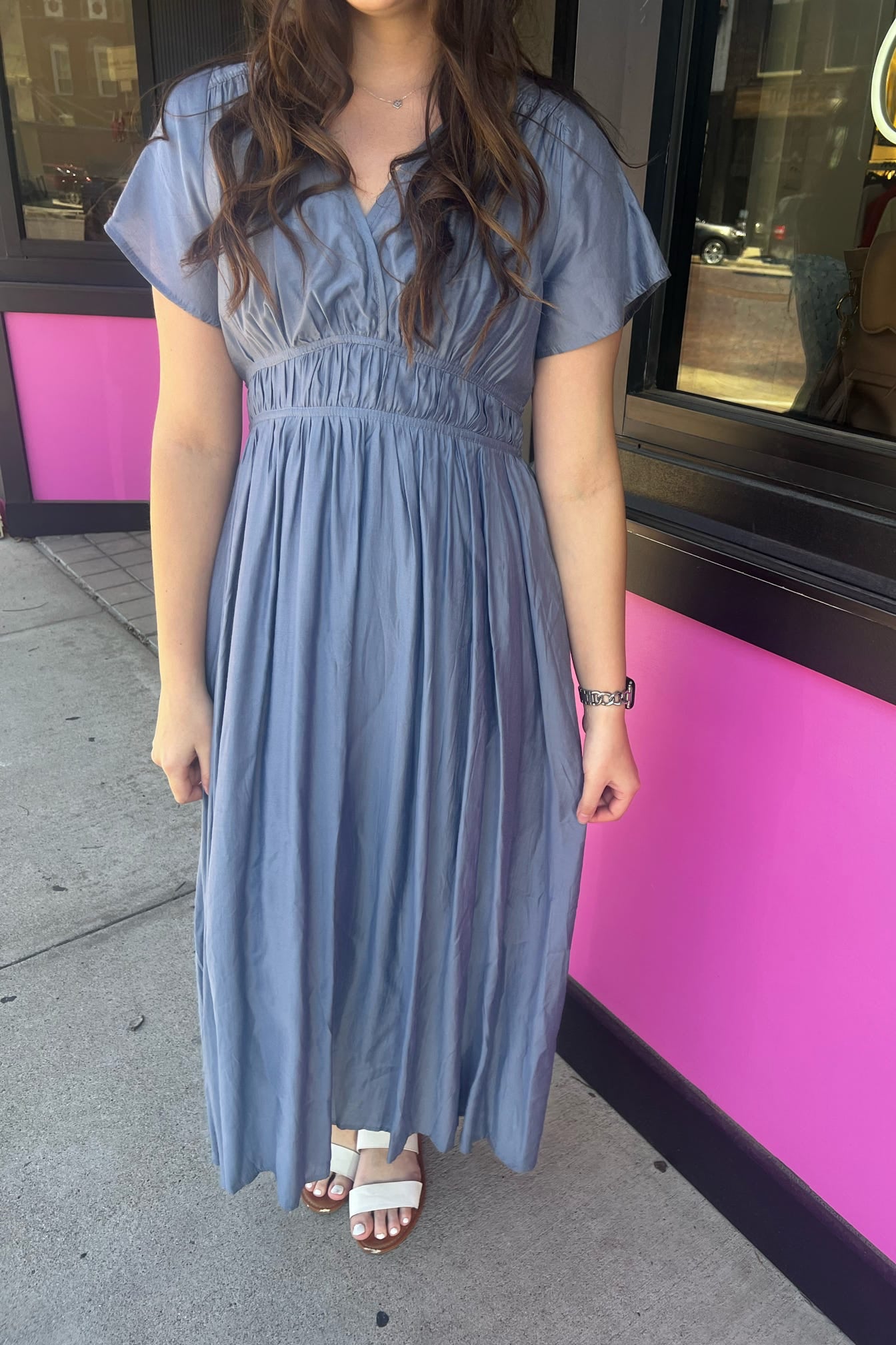 Woman wearing a blue dress standing in front of a pink building.