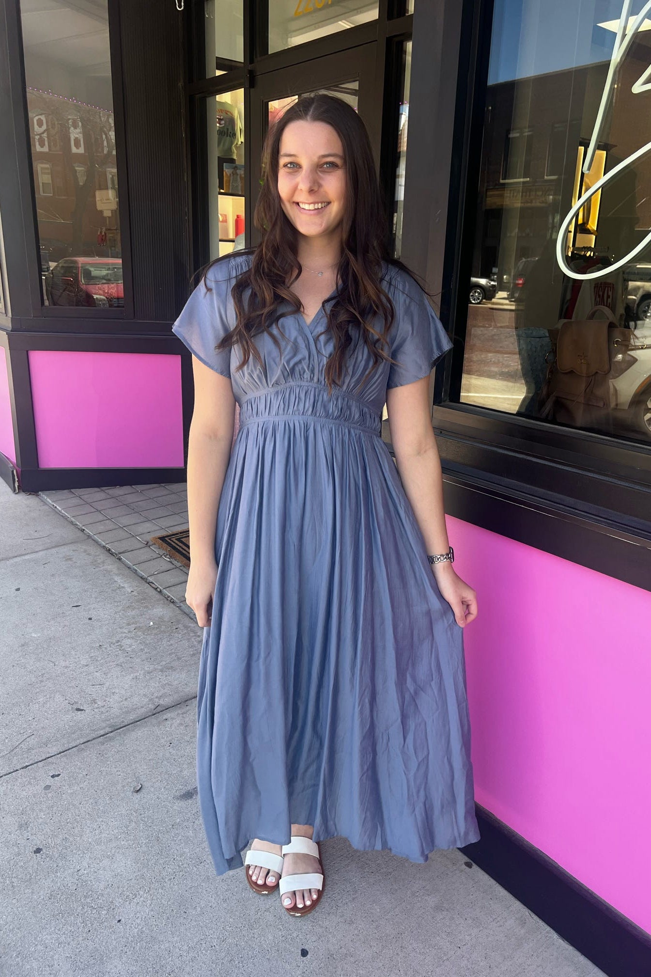 Woman in a blue dress standing on a sidewalk with a pink building in the background