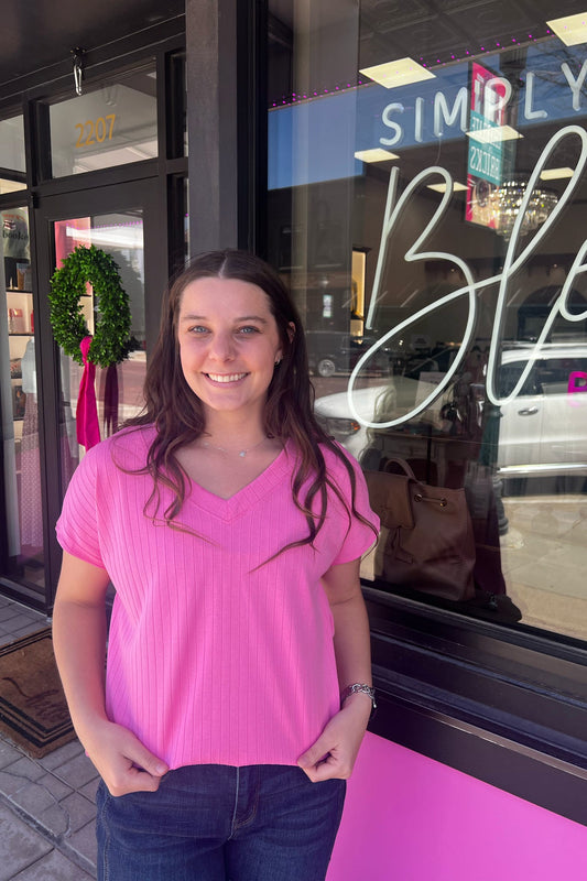 Woman in a pink shirt standing outside a store with a neon sign.