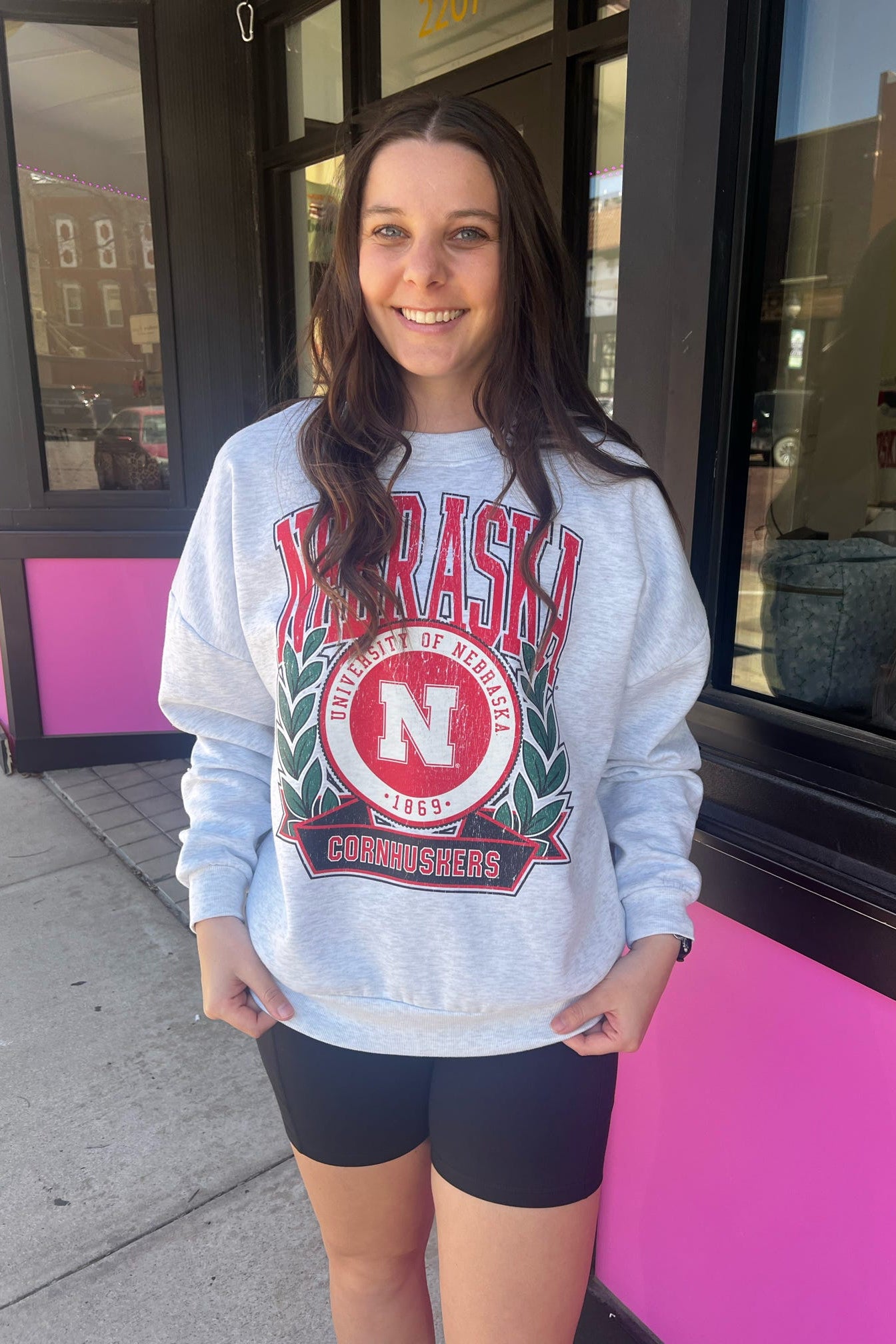 Woman wearing a Nebraska sweatshirt standing outside a building with a pink door.