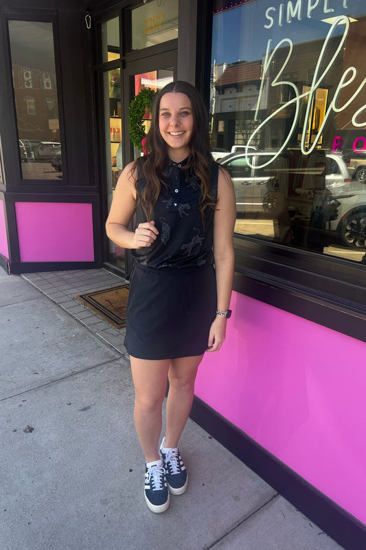 Woman in a black outfit standing on a sidewalk in front of a store with pink and purple exterior.