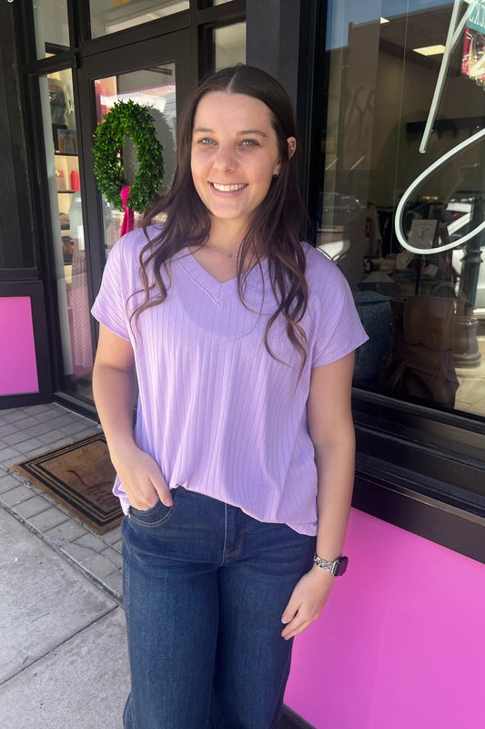 Woman in a purple shirt standing outside a store with pink entrance.