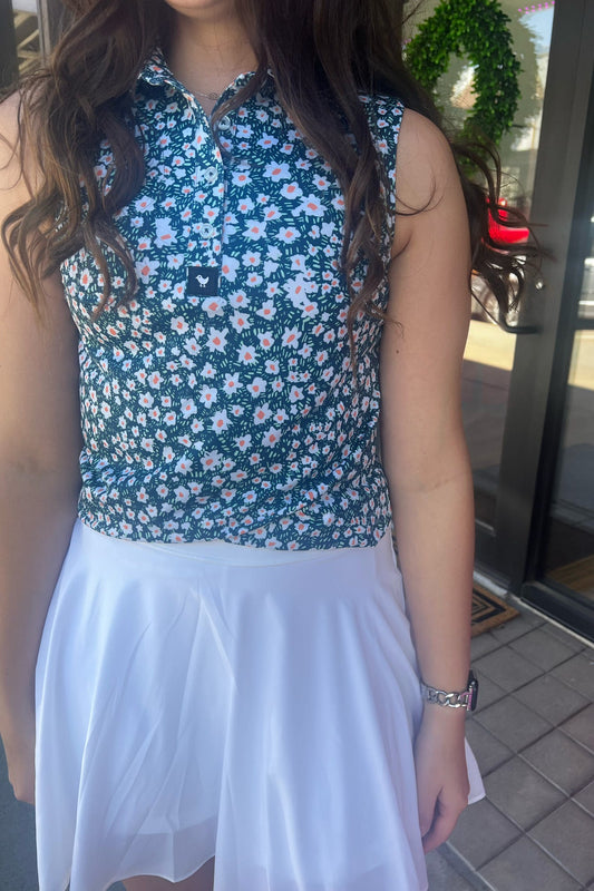 Person wearing a blue floral sleeveless top and white skirt outdoors.