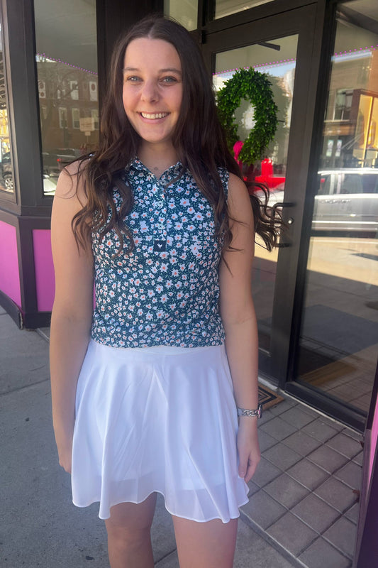 Woman in a floral top and white skirt standing outside a building with a pink and black exterior.