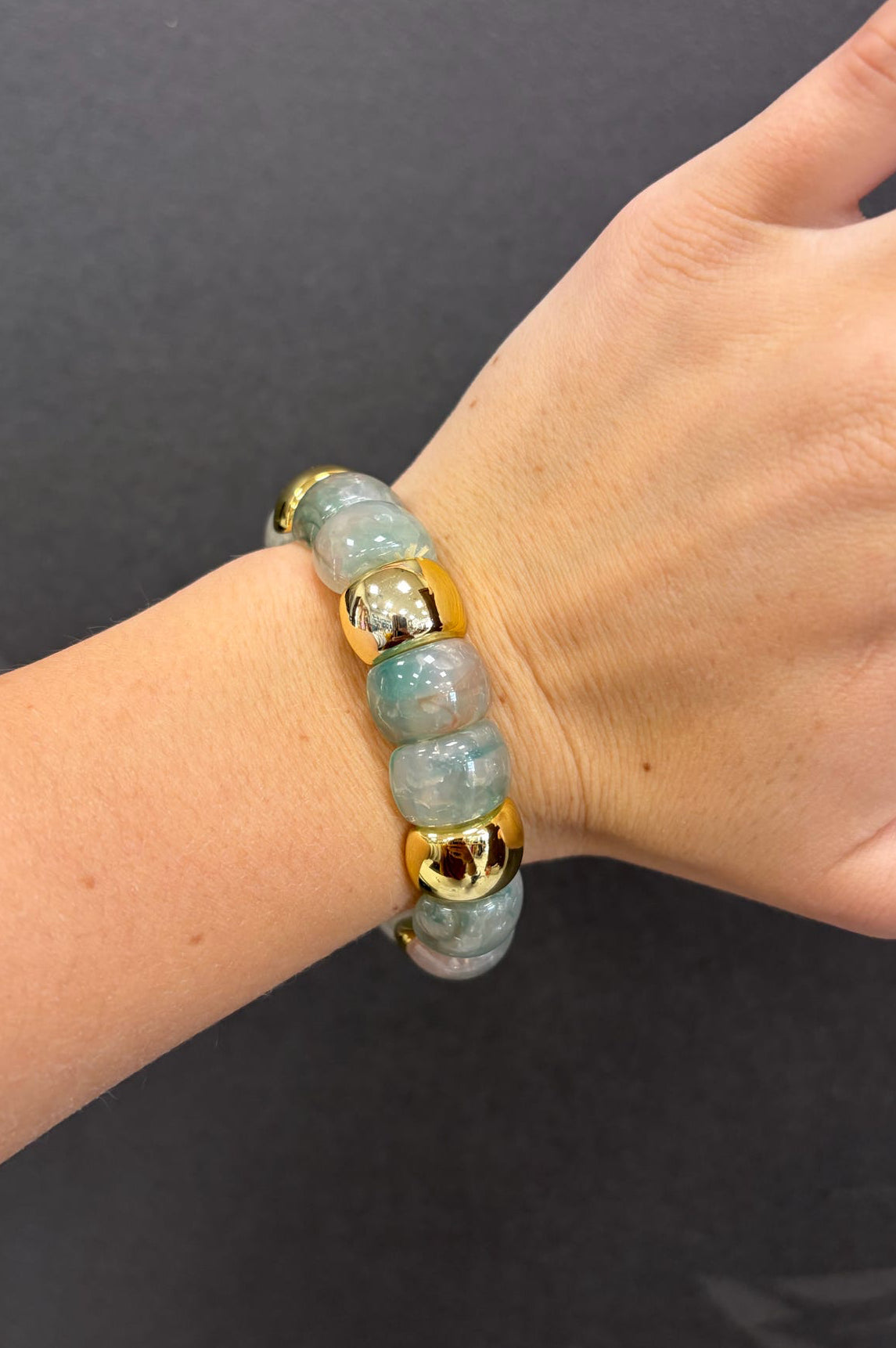Hand wearing a bracelet with blue beads and gold accents on a dark background
