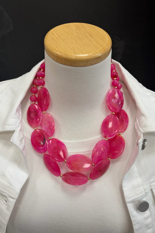 Mannequin wearing a bright pink beaded necklace with a white jacket.