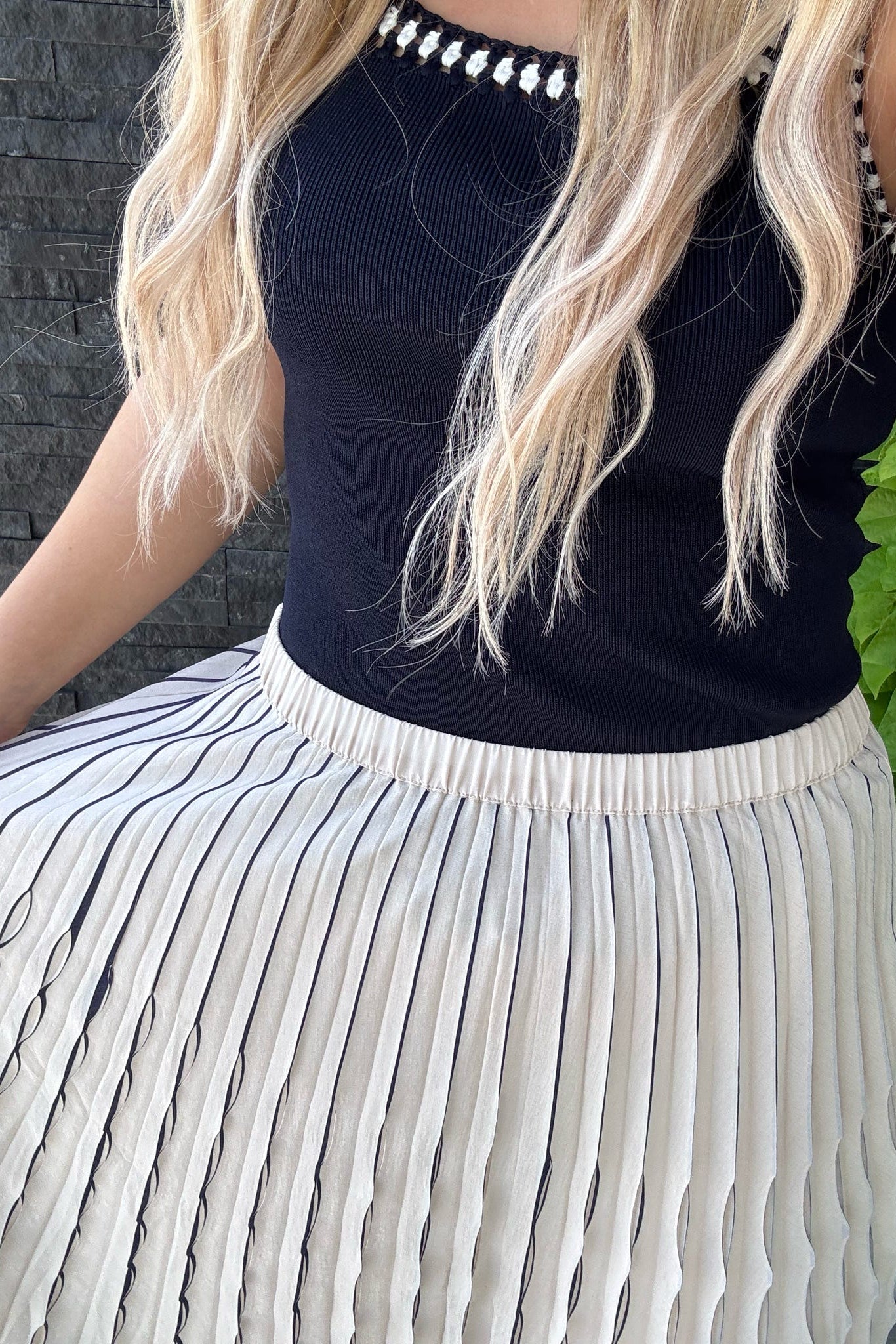 Person wearing a navy sleeveless top and pleated skirt with a blurred background