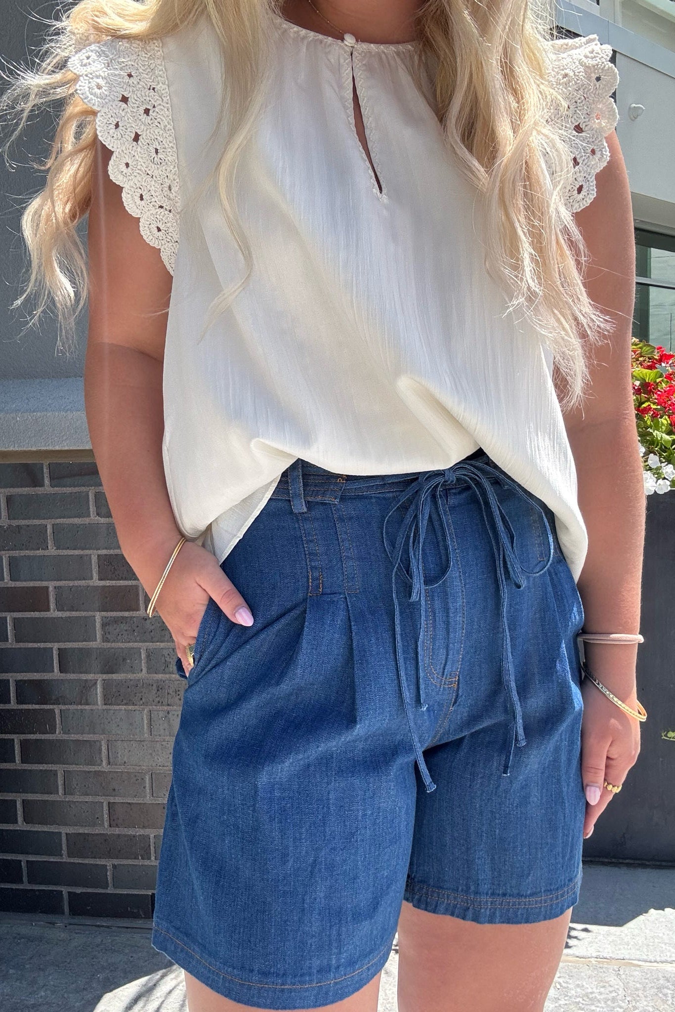 Woman wearing a white blouse with lace details and blue denim shorts outdoors.