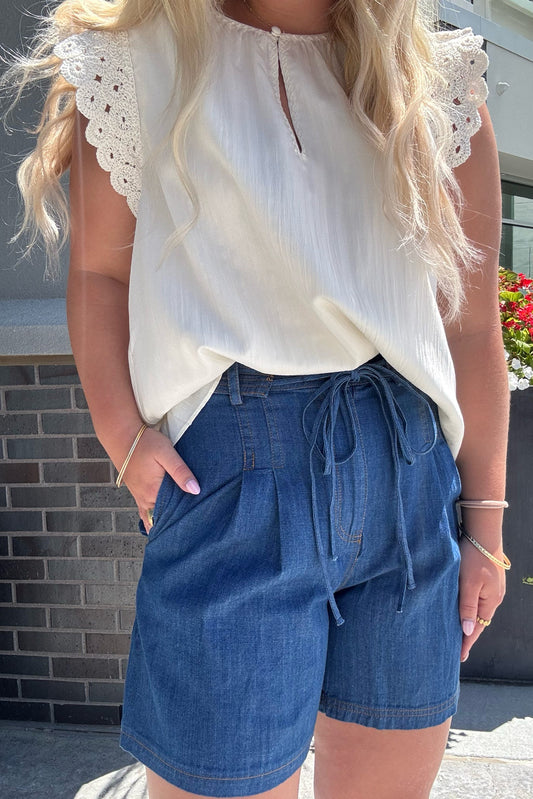 Woman wearing a white blouse with lace details and blue denim shorts outdoors.