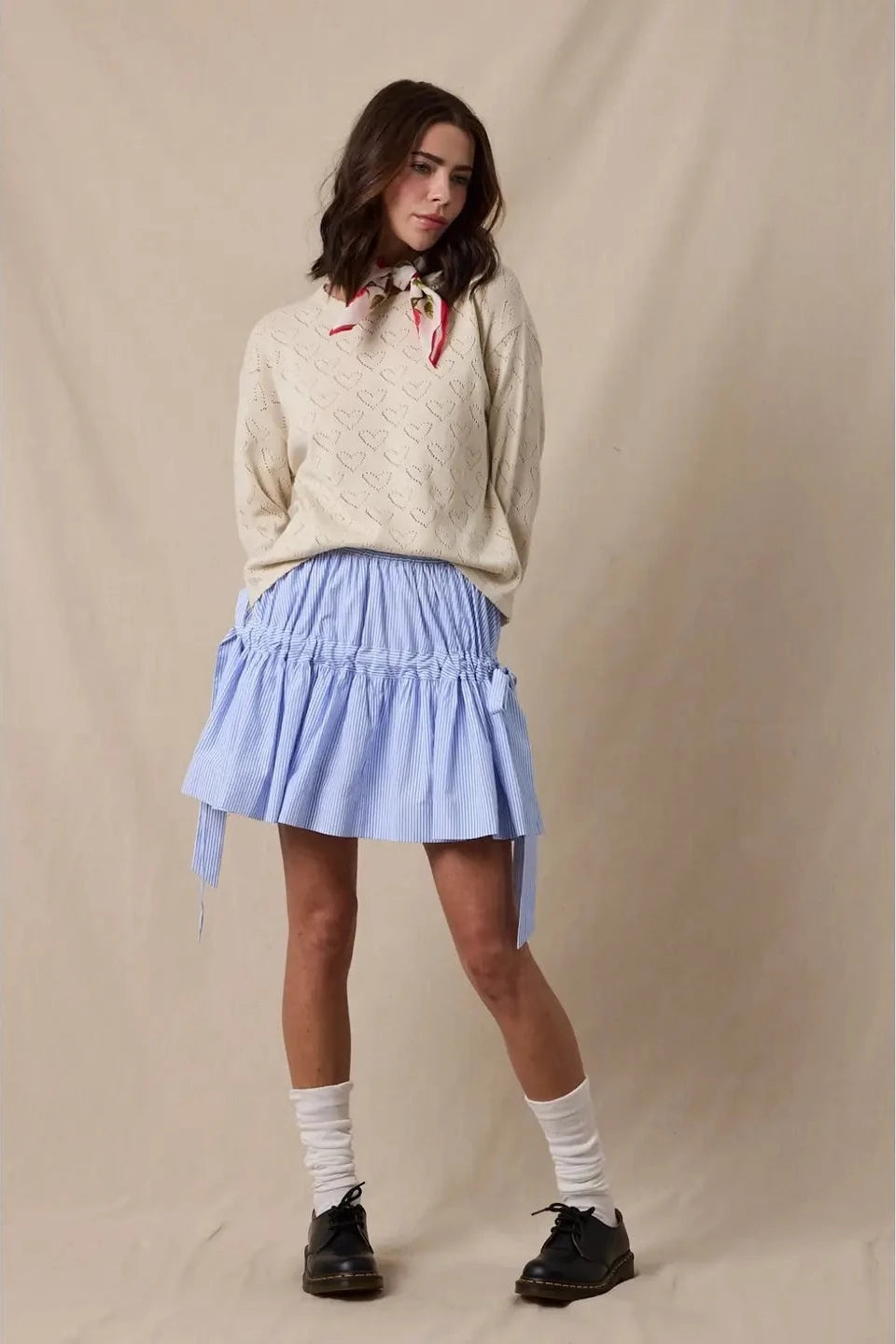 Woman wearing a beige sweater and light blue skirt against a beige background