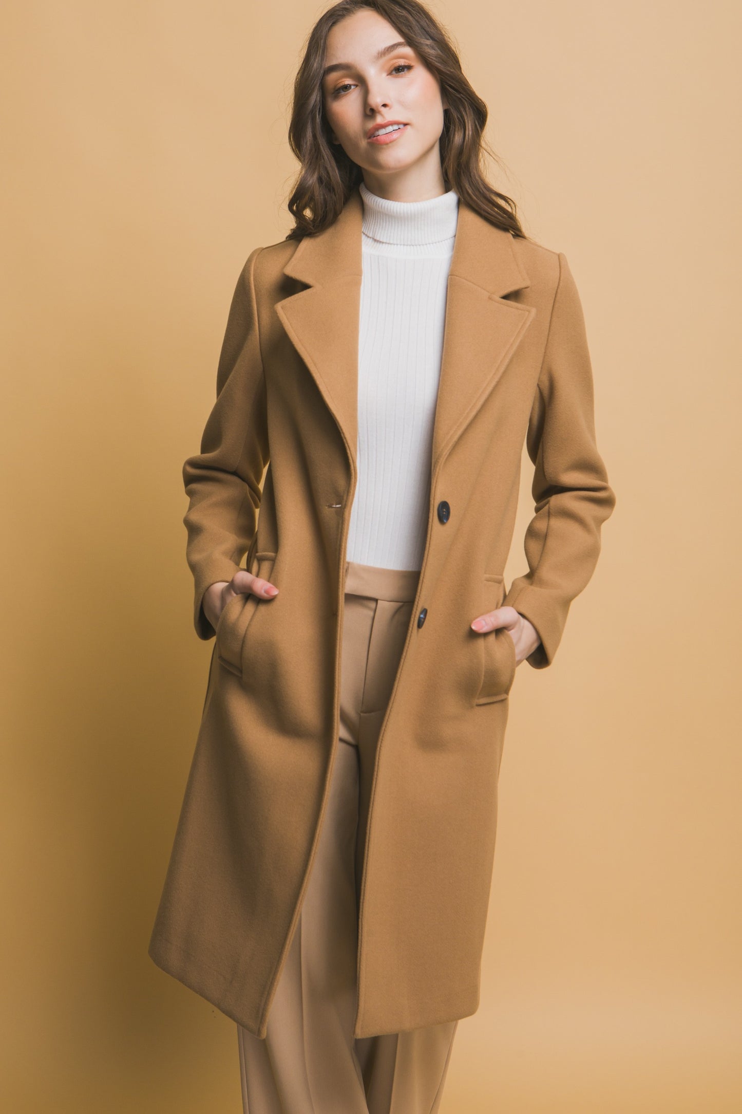 Woman wearing a brown coat and beige pants against a beige background