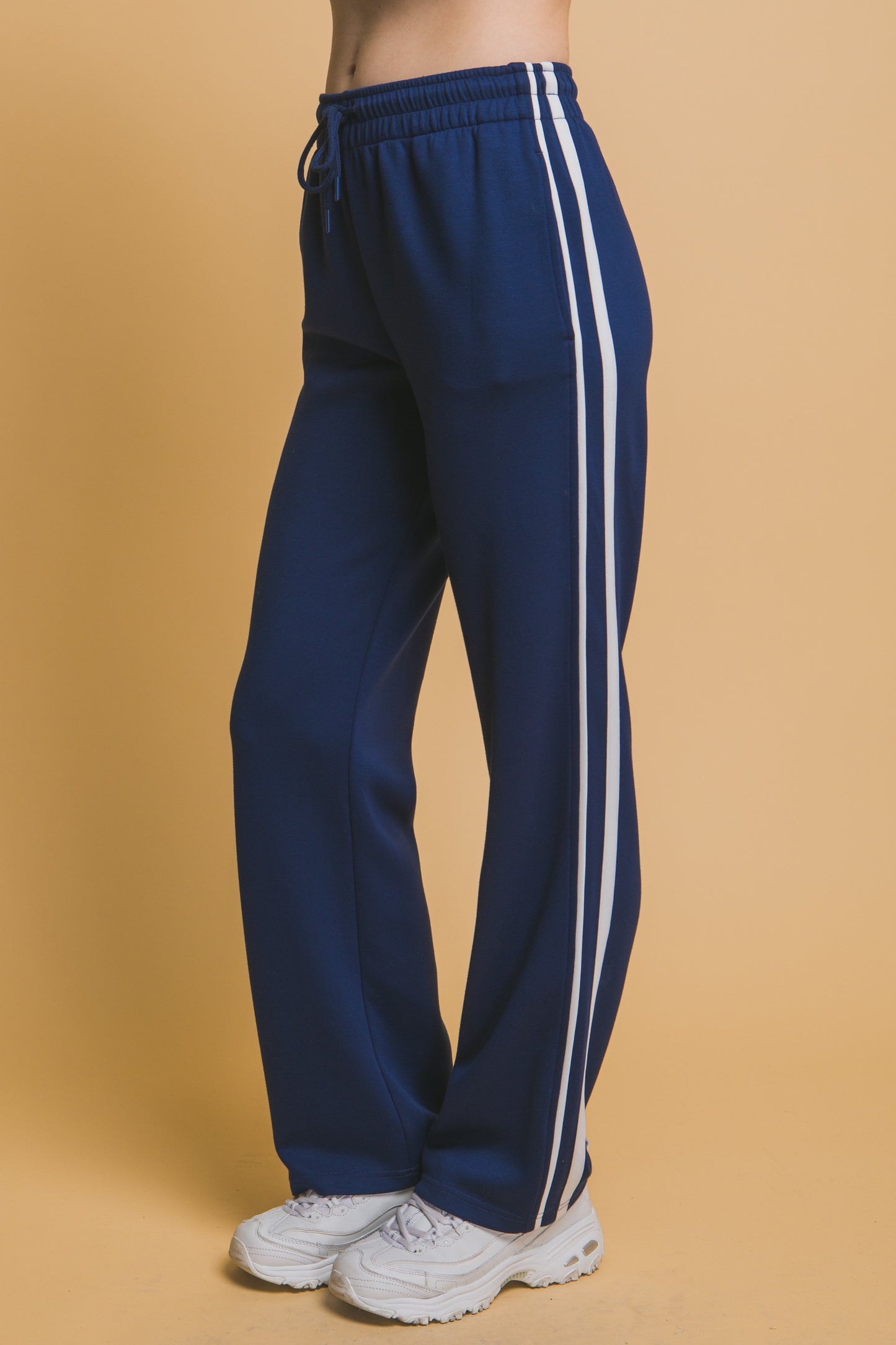 Navy blue track pants with white stripes on a beige background