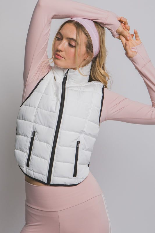 Woman wearing a white puffer vest over a pink long-sleeve top and leggings on a light gray background