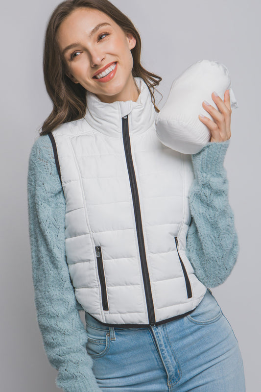 Woman wearing a white puffer vest over a light blue sweater, holding a white mug.