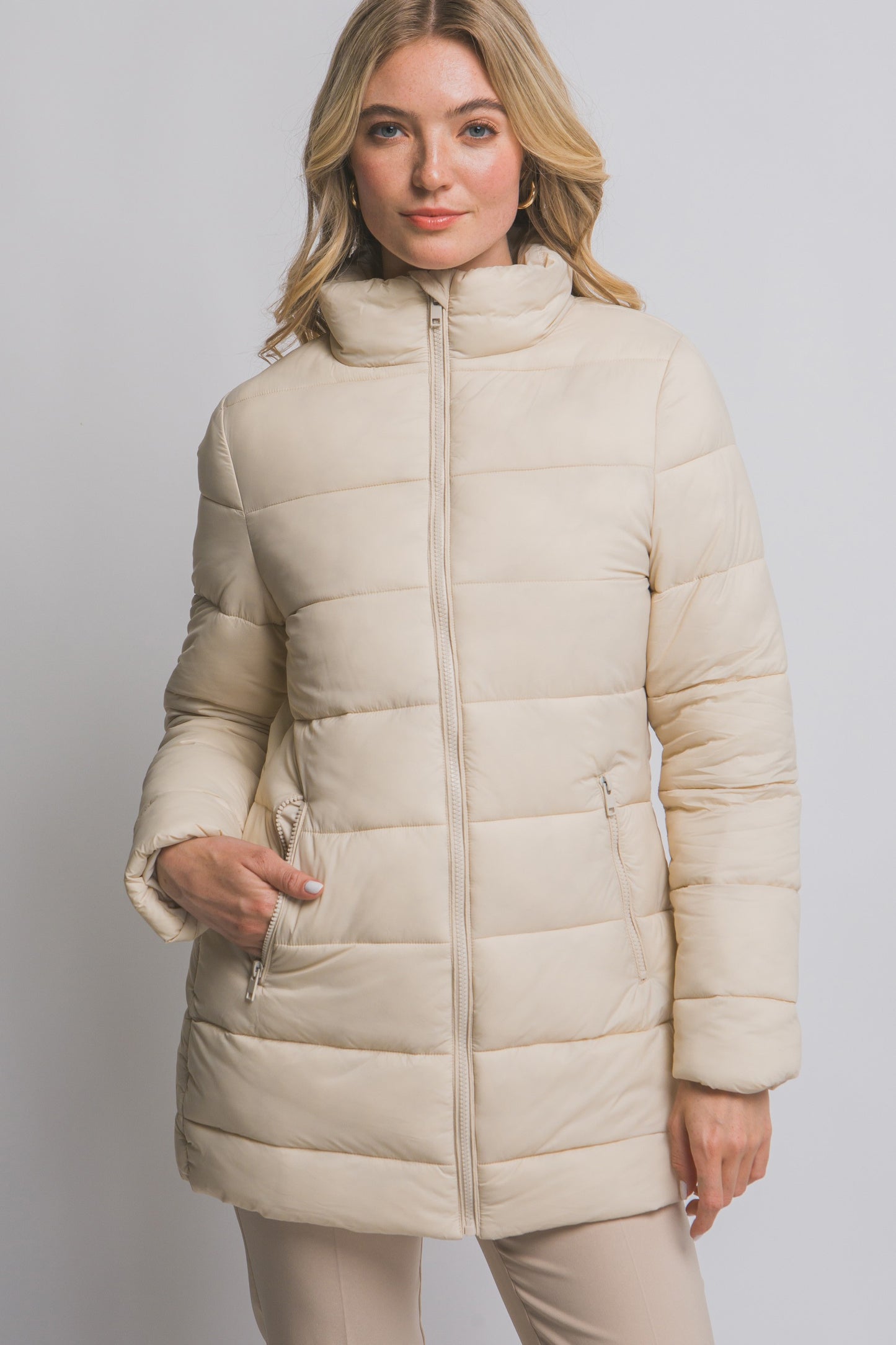 Woman wearing a beige puffer coat against a plain background