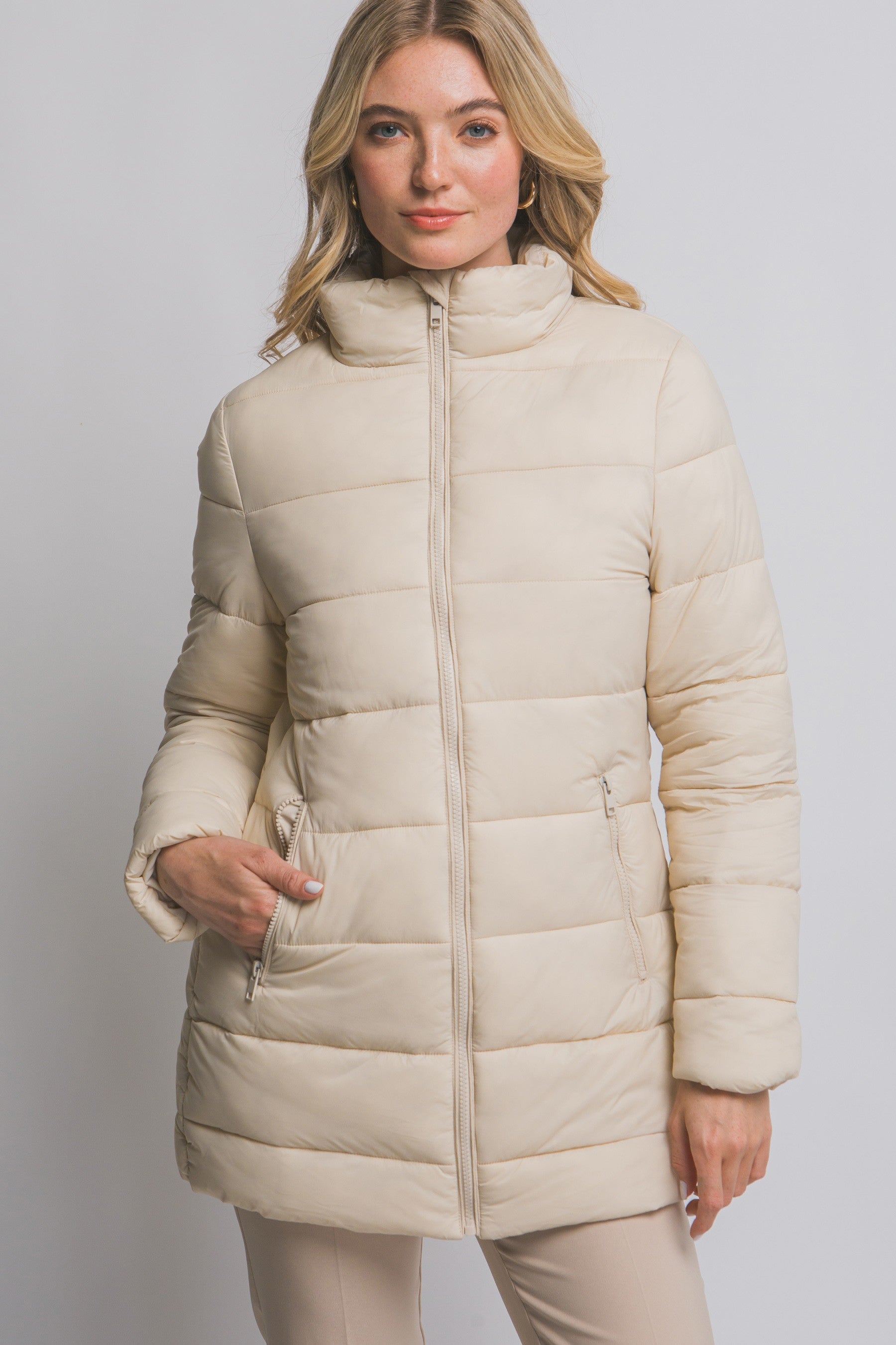 Woman wearing a beige puffer coat against a plain background