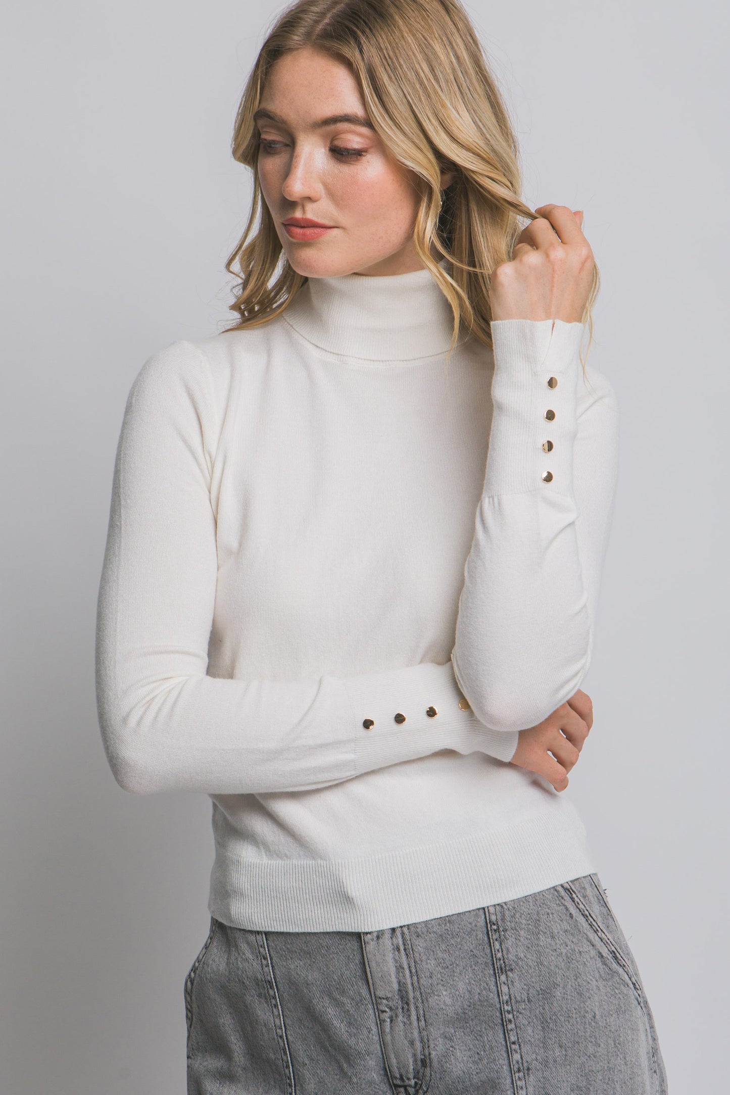 Woman wearing a white turtleneck sweater with button details on a plain background