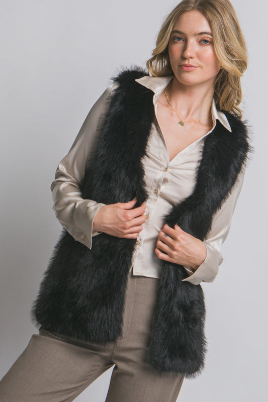 Woman wearing a black fur vest over a cream shirt on a plain background