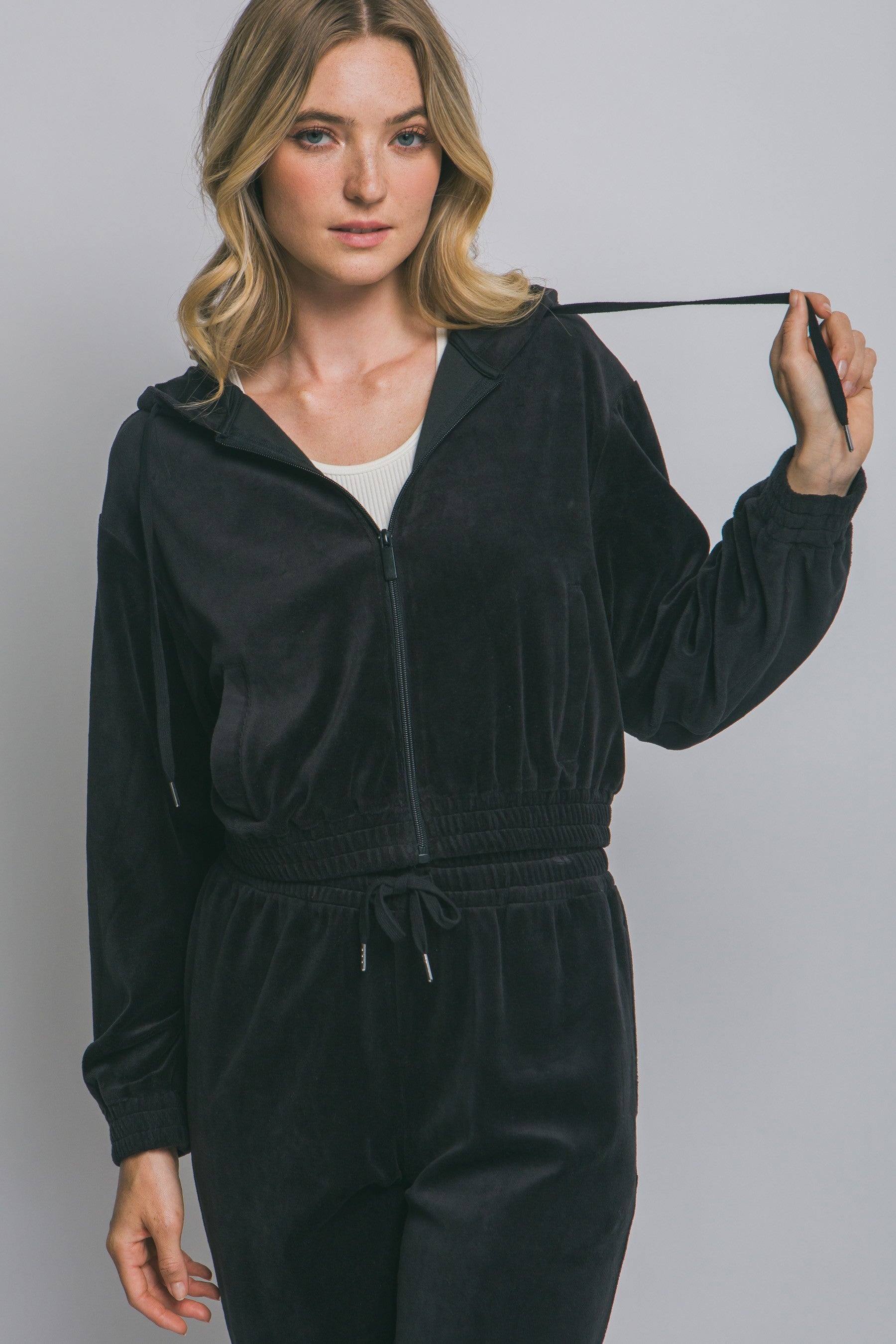 Woman wearing a black tracksuit holding a measuring tape against a gray background