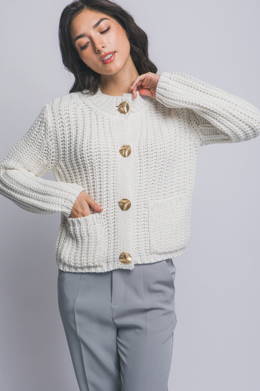 Woman wearing a white knitted cardigan with gold buttons on a gray background