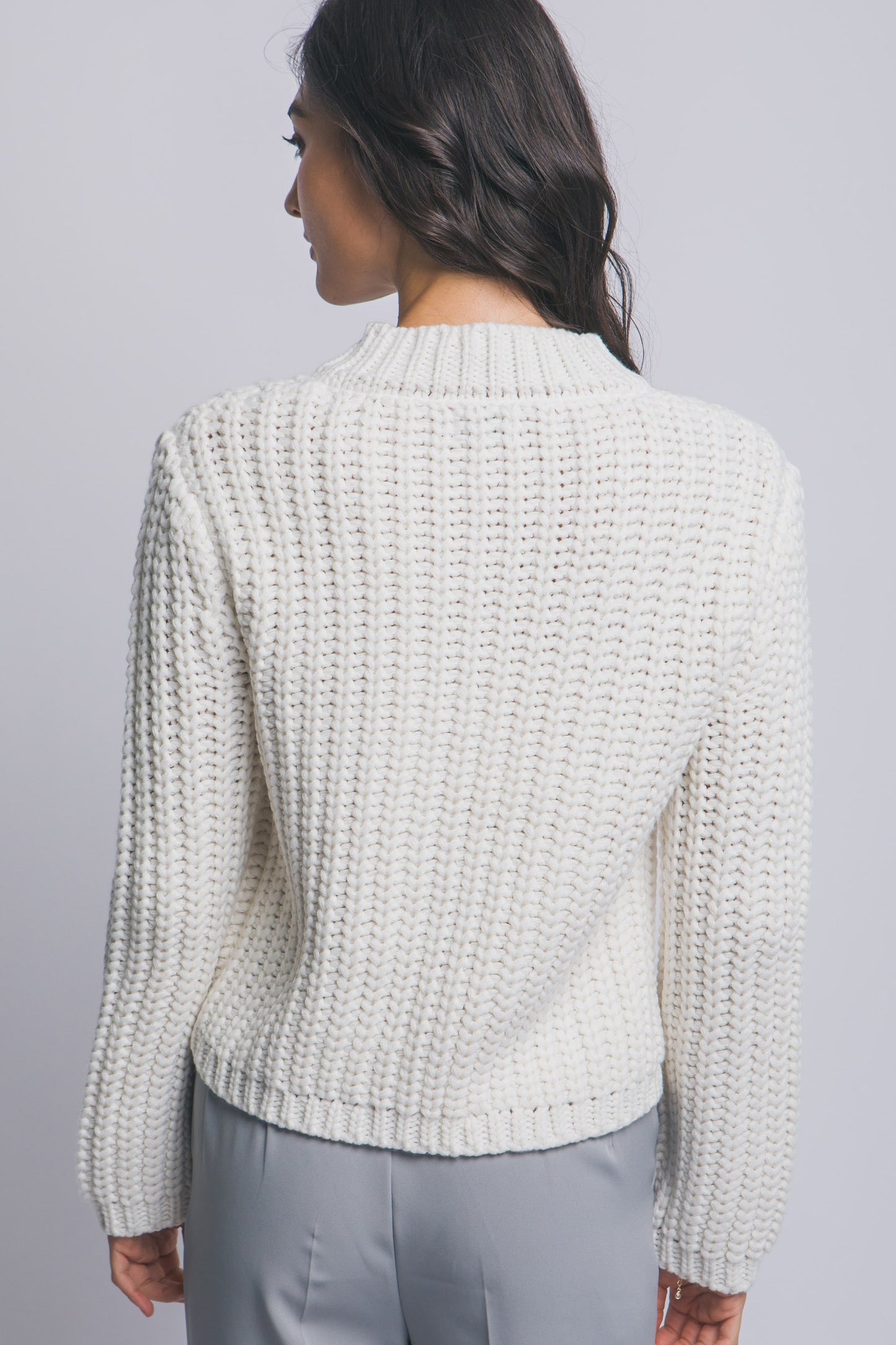 Woman wearing a textured light gray sweater against a plain background