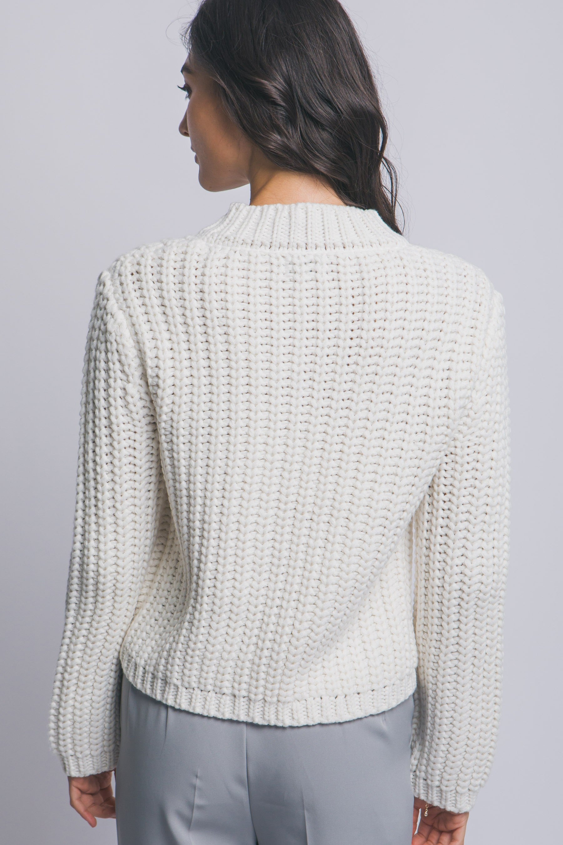 Woman wearing a textured light gray sweater against a plain background